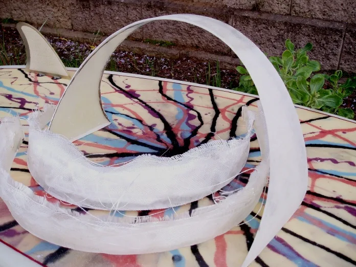 Raw fiberglass hoop fin arcing over a resin-swirl board during construction